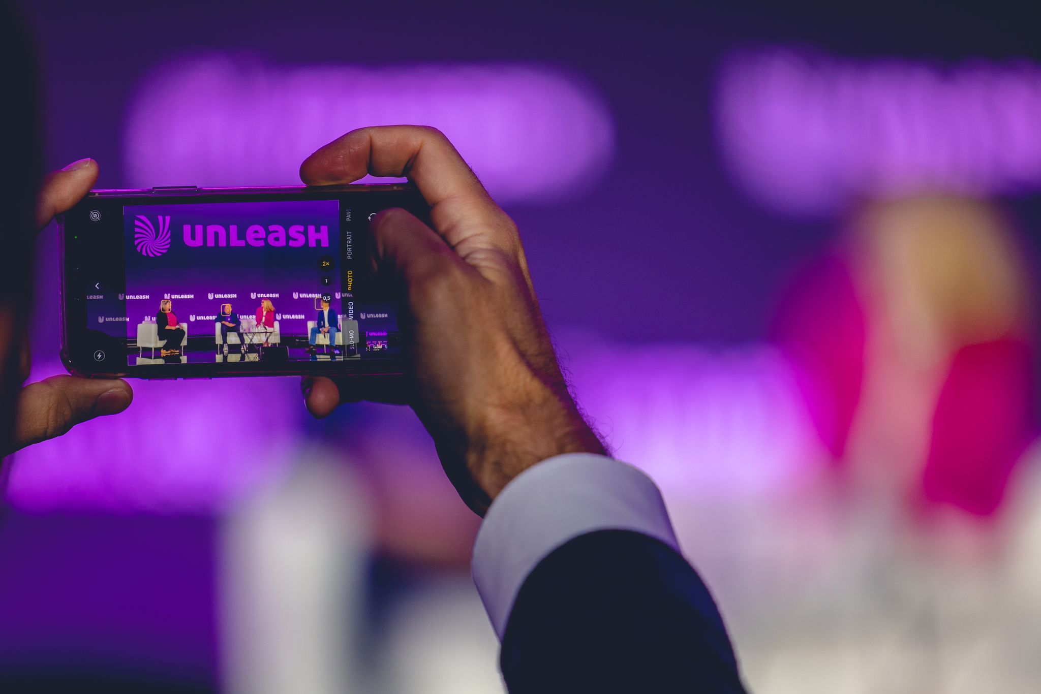 A pair of hands taking a picture of the UNLEASH America Stage with the UNLEASH logo showing on the screen.